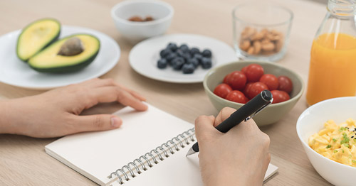 A person taking notes with food on a table.