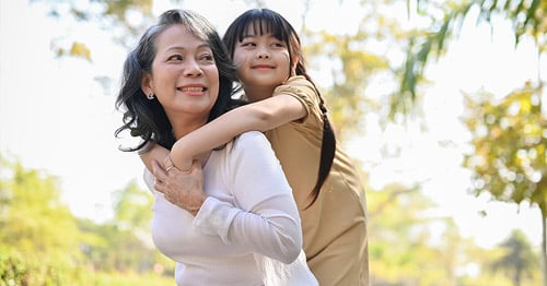 A smiling, active older woman giving her granddaughter a piggyback ride.