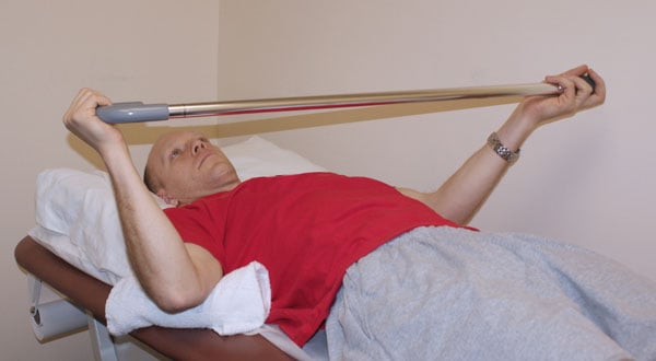 Man lying prone holding a cane with both arms.