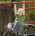 Photo of a child hanging from monkey bars at the park