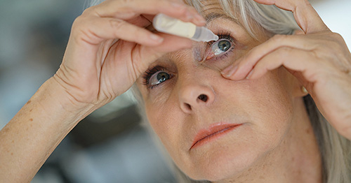 An older woman using eyedrops.