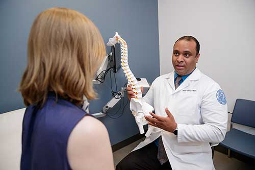 a doctor holds a spine model while talking to a patient