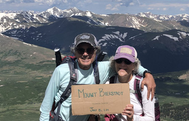 Man and woman at summit of mountain displaying cardboard sign that says Mount Bierstadt