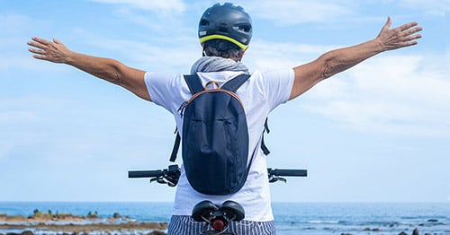 An older person on a bicycle stretching out the arms free of pain.