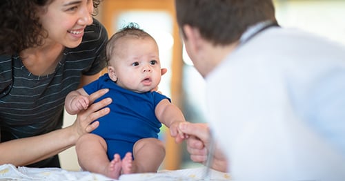 Mother holding a baby before a doctor.