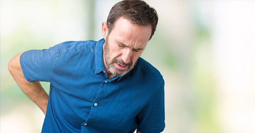 A middle aged man holding his lower back in pain.