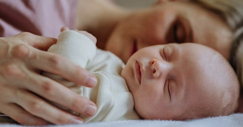 A mother cuddling with a sleeping newborn baby.