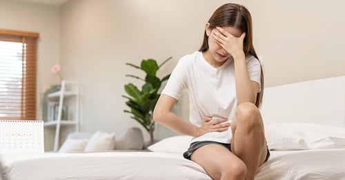A teenage girl holding her head and abdomen in pain.