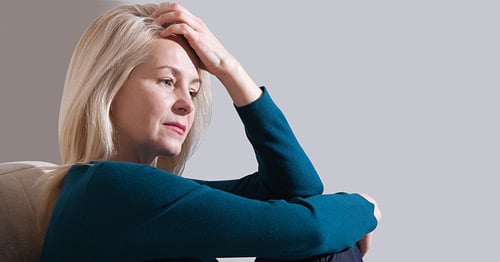 A woman holding her head pensively with a pained expression.