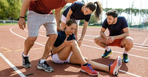 A young woman sitting on a runner's track experiencing knee pain.