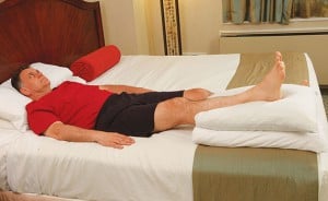 image of man laying in bed with right leg propped on pillows