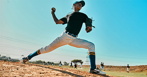 A teenage baseball pitcher cocking in a pitch.