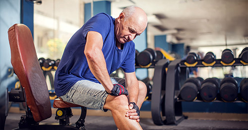 An older man feeling knee pain at the gym.