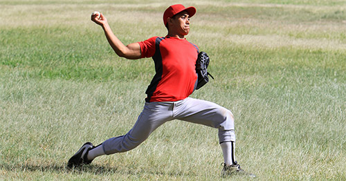 A young male baseball pitcher cocking in a pitch.