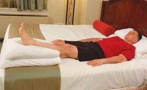 image of man laying in bed with left leg propped on pillows